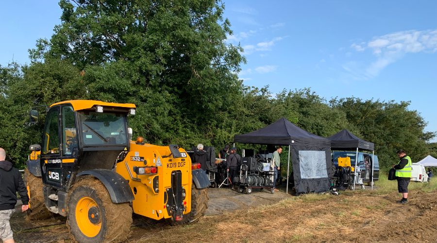JCB loader with tents and filming equipment set up on a farm